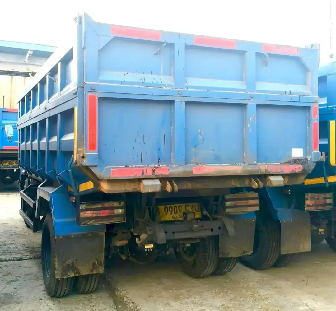 Dump truck berwarna biru tampak belakang di area armada.