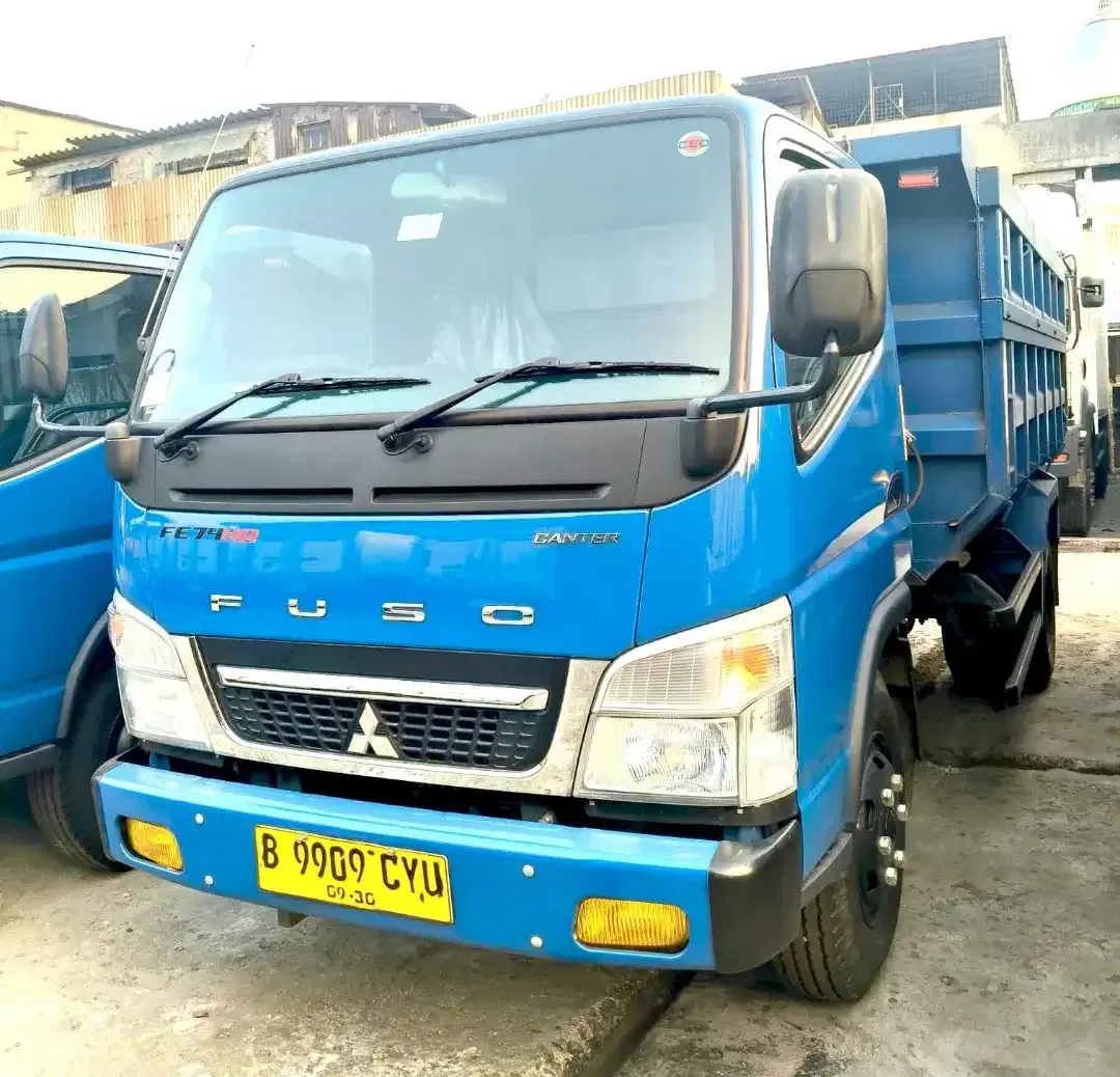 Armada dump truck Mitsubishi Fuso berwarna biru tampak depan.