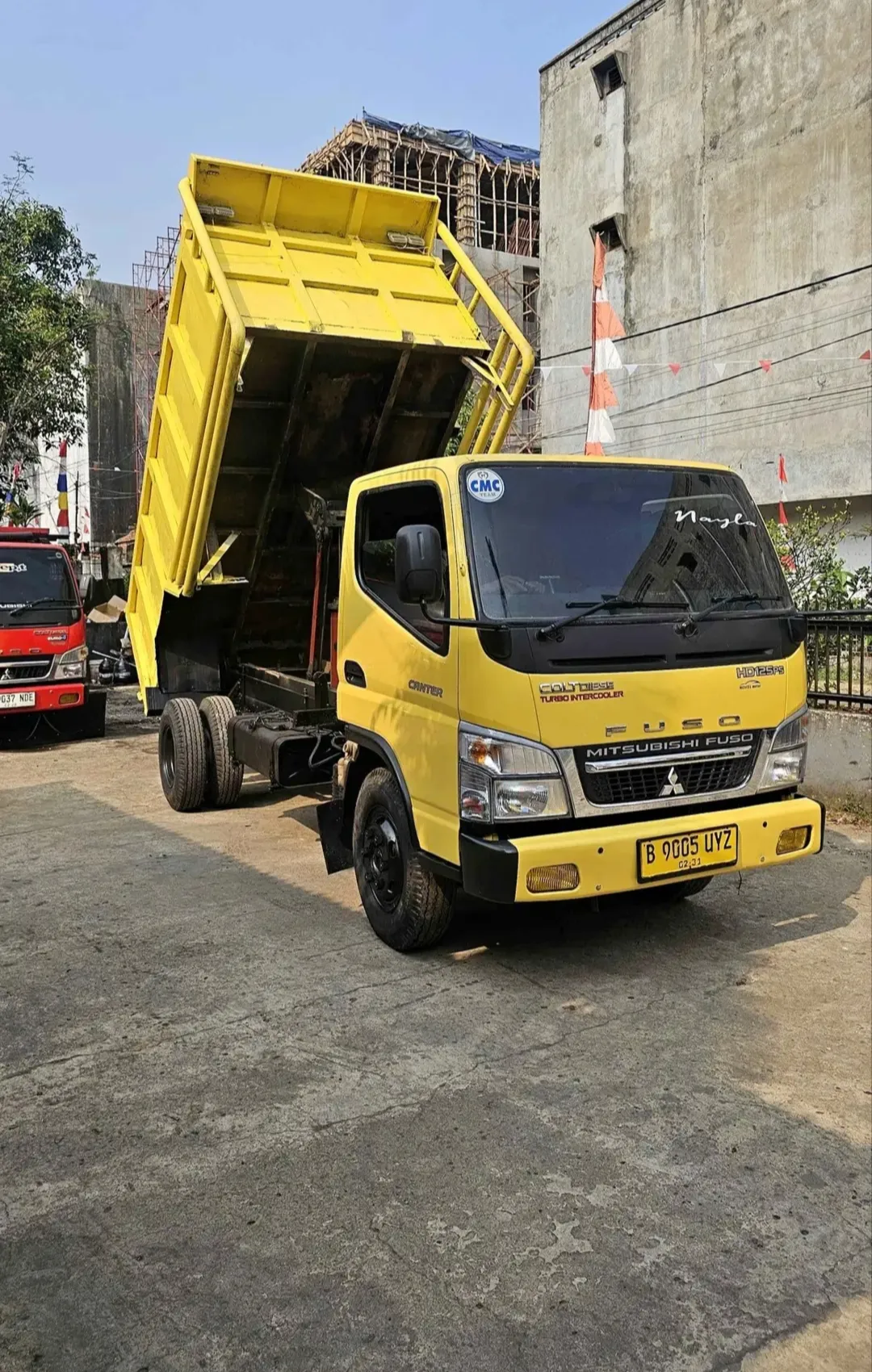 Dump truck Mitsubishi Fuso berwarna kuning dengan bak terangkat.