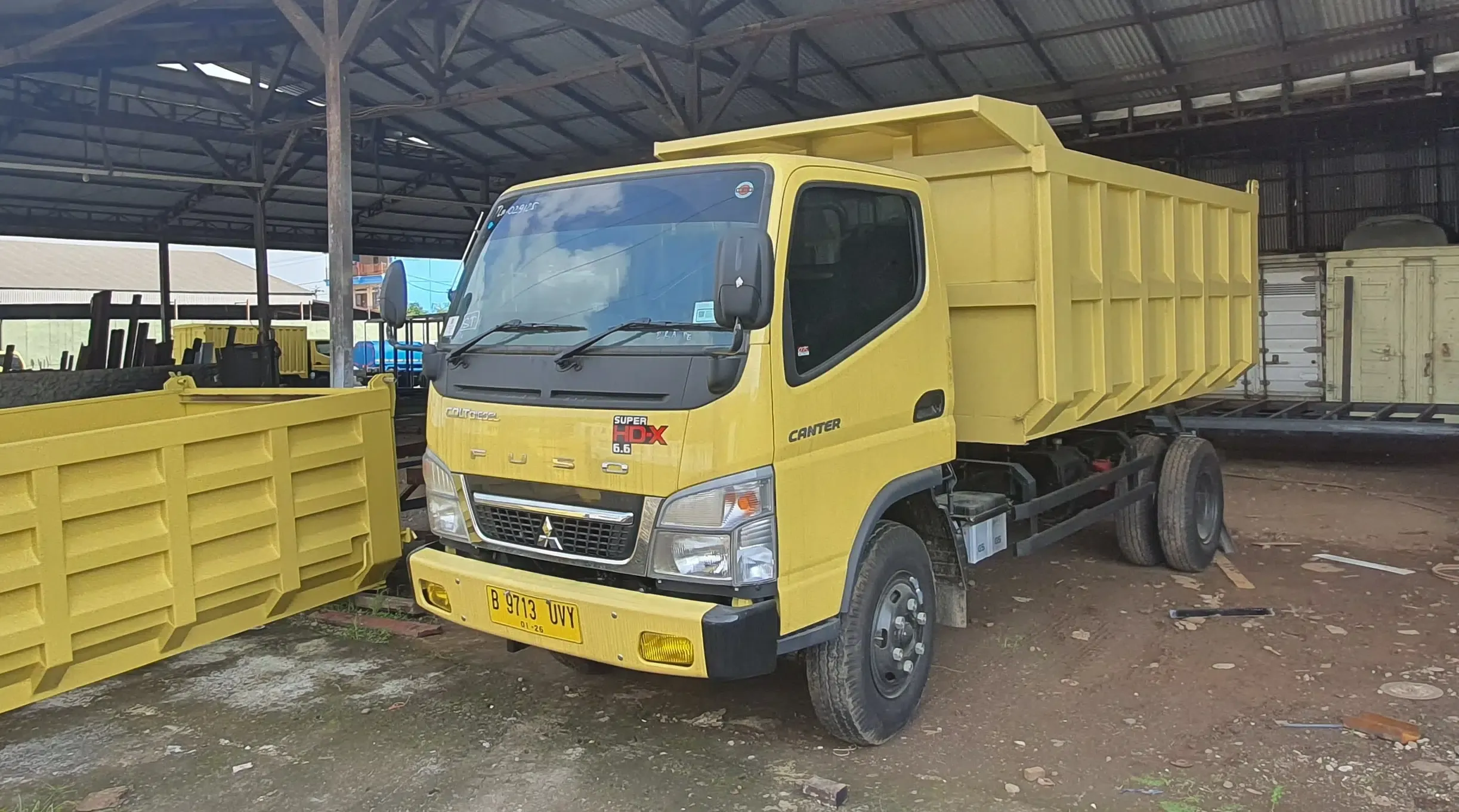 Armada dump truck Mitsubishi Fuso berwarna kuning di garasi.