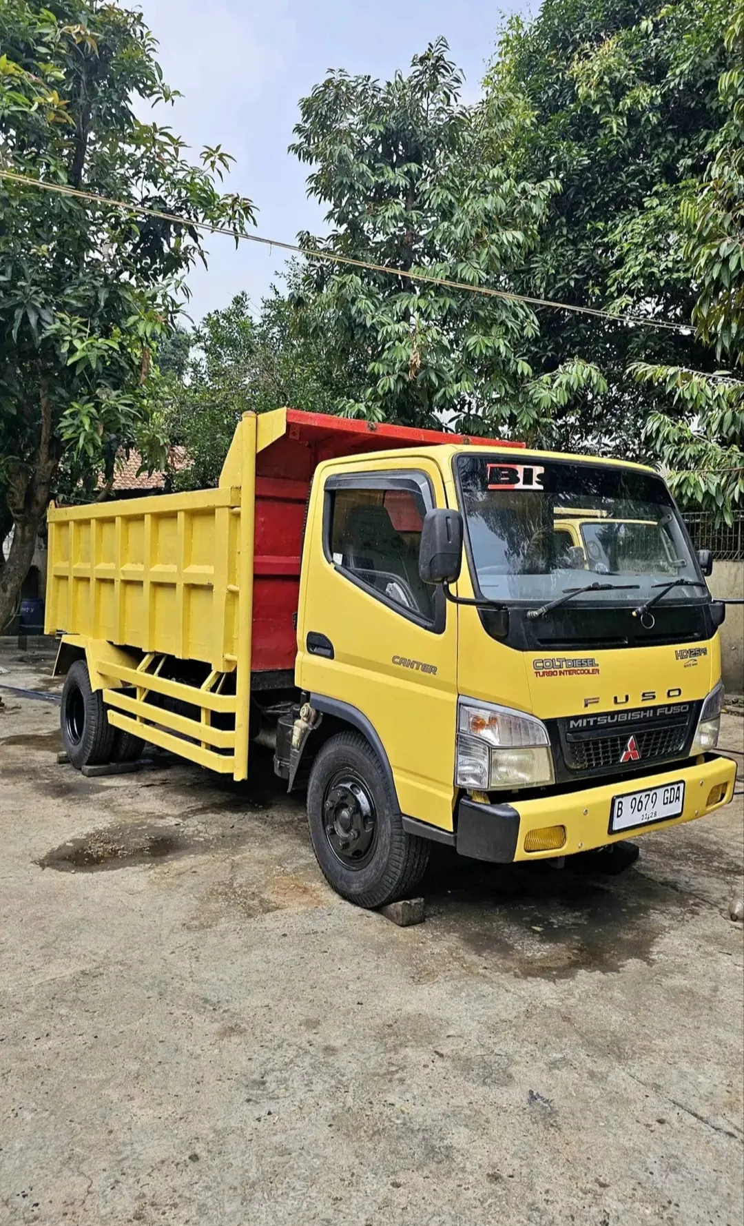 Dump truck Mitsubishi Fuso kuning dengan bak merah tampak dari samping.