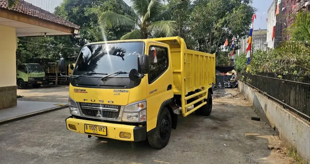 Dump truck Mitsubishi Fuso berwarna kuning tampak dari sisi depan.