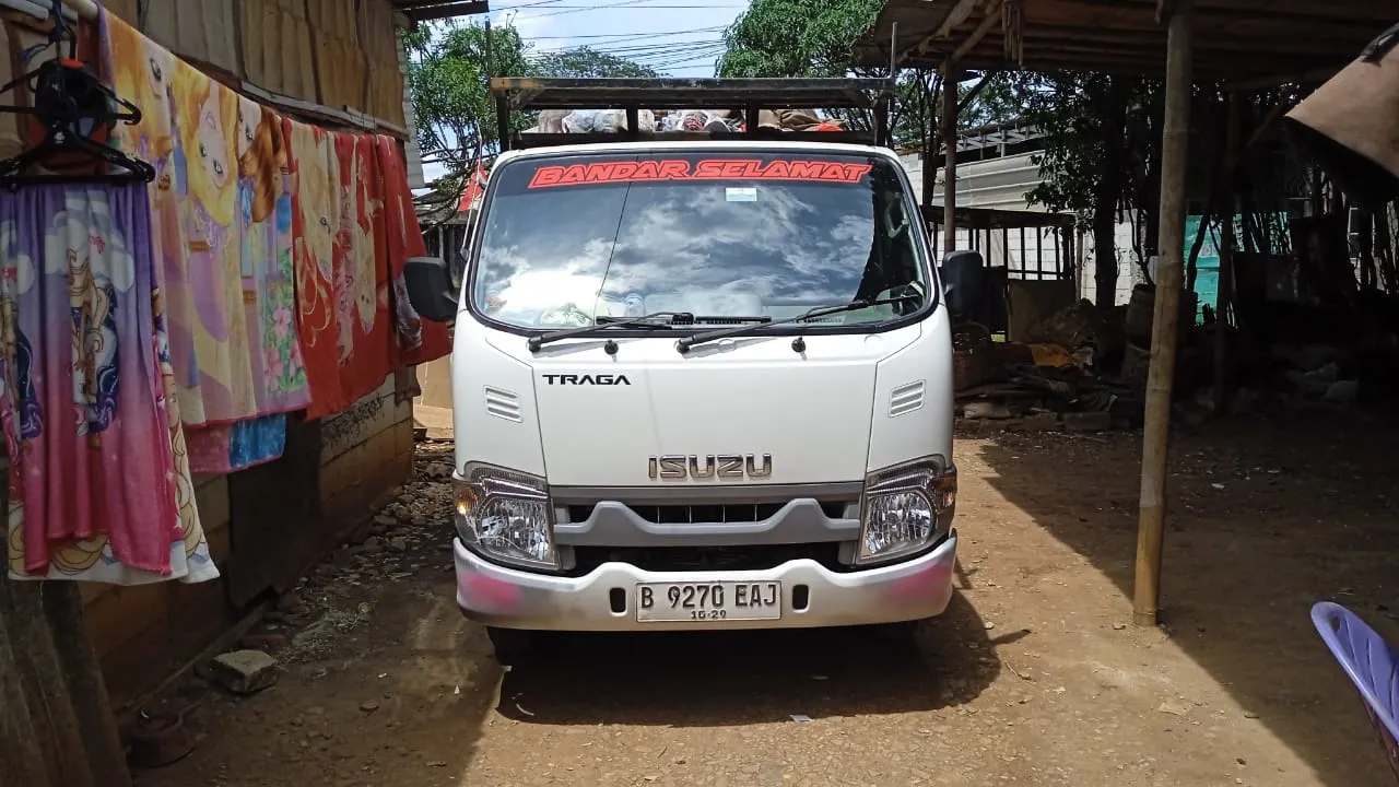 Armada Isuzu Traga putih tampak dari sisi depan di area operasional.