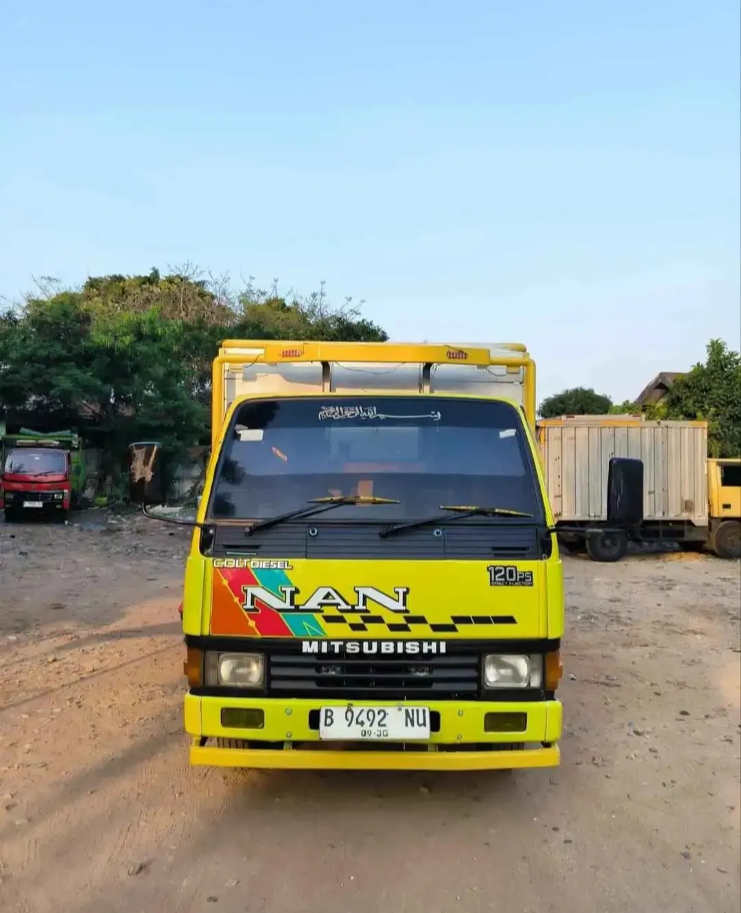 Truk angkutan berwarna kuning tampak depan di area armada.