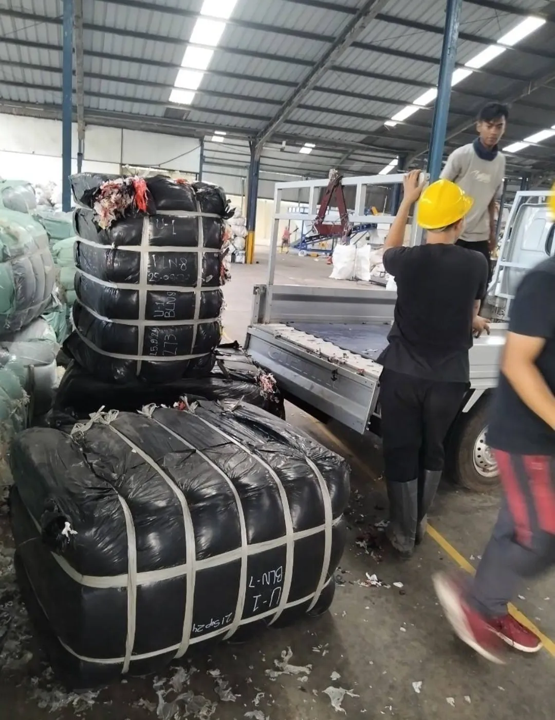 Petugas memuat bal material anorganik ke kendaraan pengangkut.